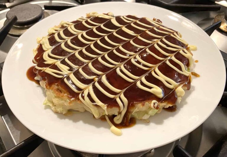 Photo of Okonomiyaki on a plate with an unfinished pattern drawn into the sauce toppings