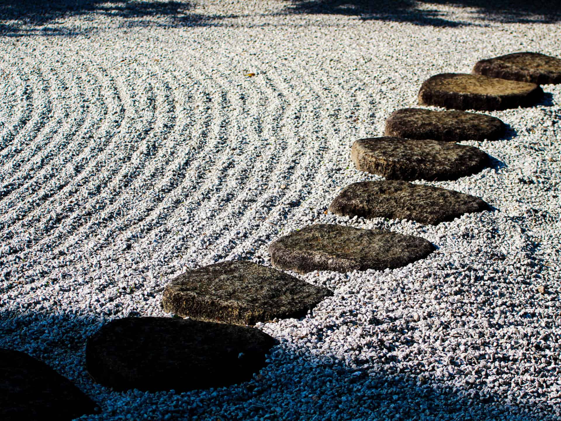 A minimalist zen garden with a series of stepping stones placed on carefully raked sand, symbolizing a path for quiet reflection.