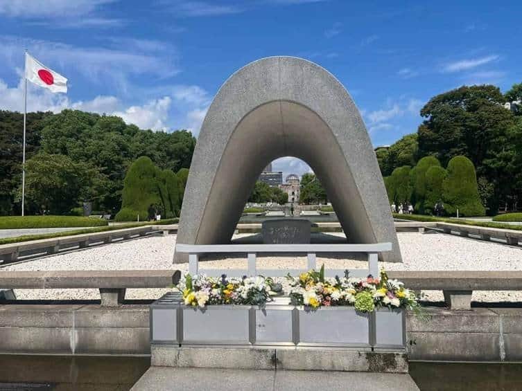The concrete saddle-shaped Cenotaph for the A-bomb Victims framing the Atomic Bomb Dome at Hiroshima Peace Memorial Park in Japan.