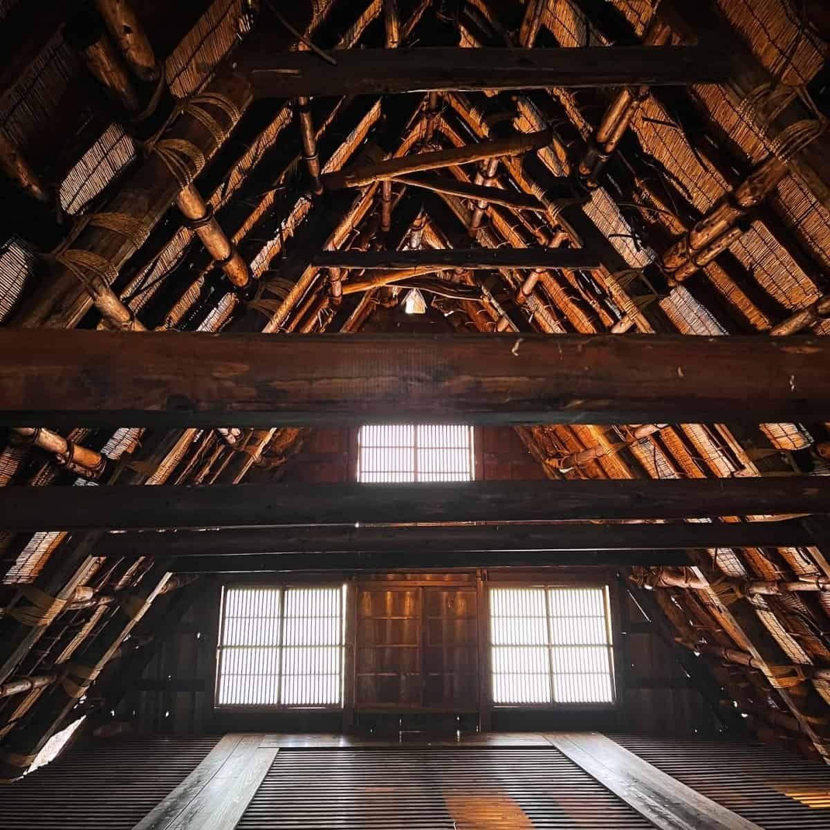 The wooden, multi-level attic interior of a traditional gassho-zukuri farmhouse, showcasing rope bindings and historic silk cultivation tools.