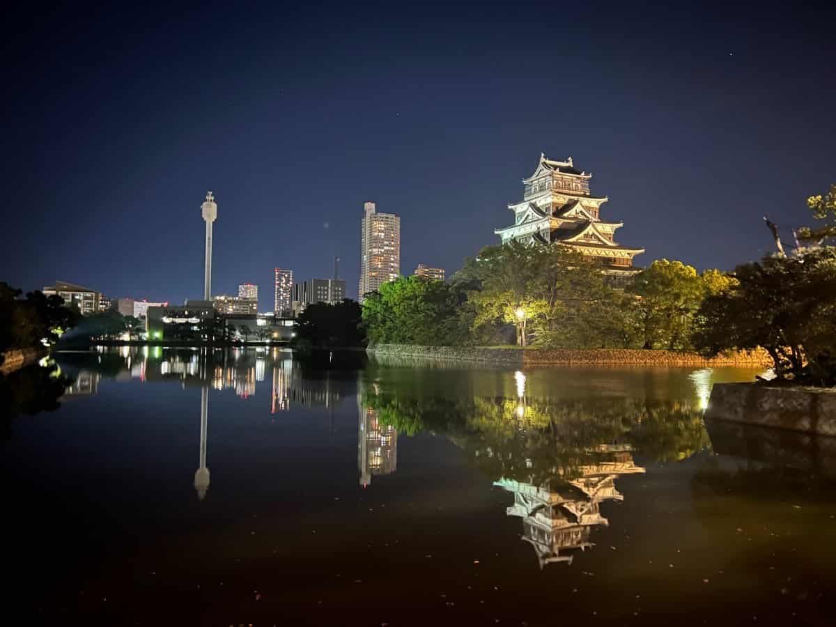 Hiroshima Castle illuminated at night with its reflection visible in the surrounding moat, showcasing the peaceful atmosphere of the city after dark