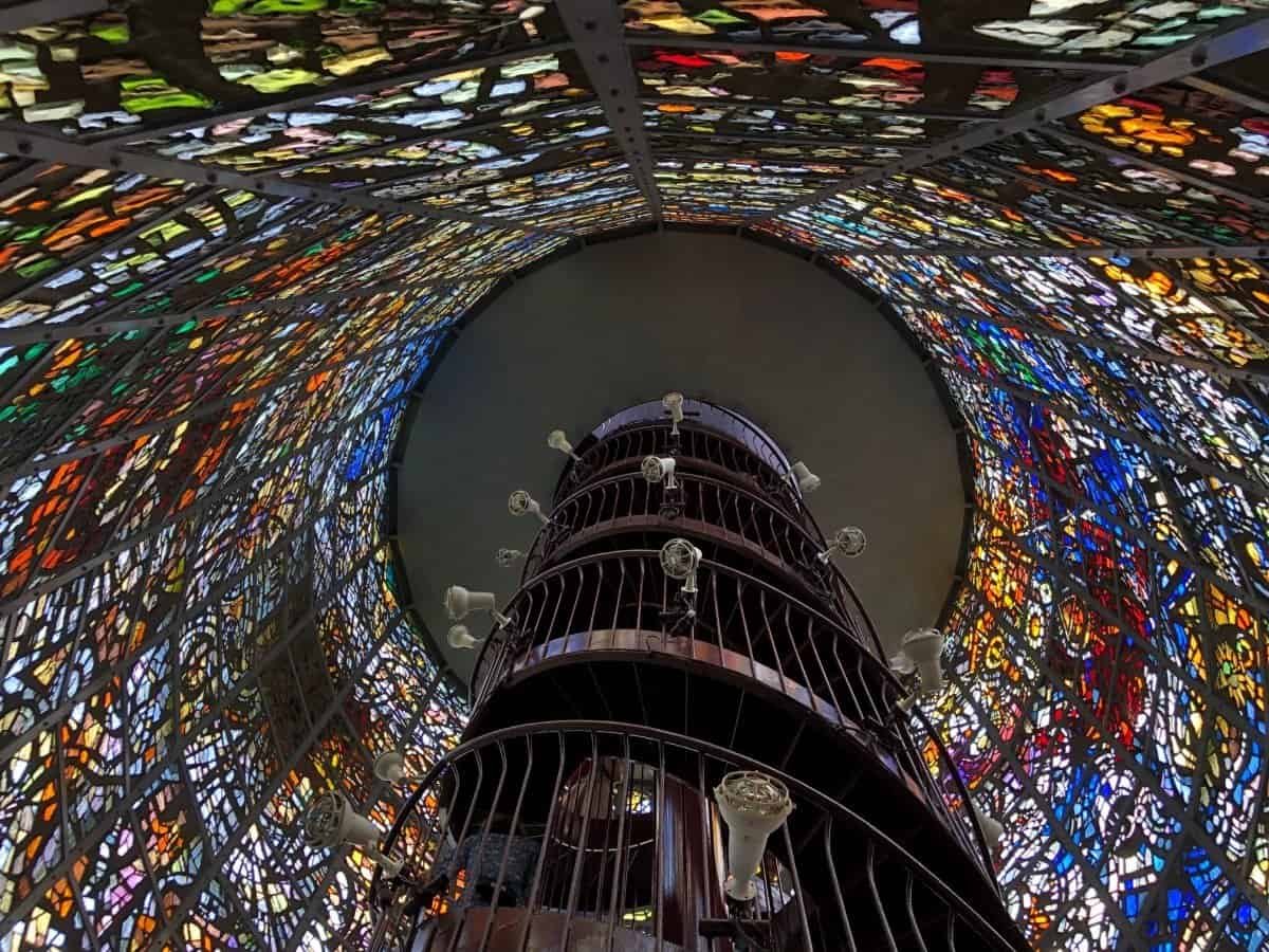 Looking straight up inside the towering stained-glass Symphonic Sculpture at the Hakone Open-Air Museum, showing the spiral staircase and colourful panels.